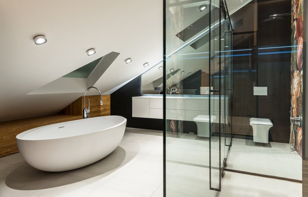 modern-bathroom-interior-with-bathtub-and-toilet-bowl-at-home-7045310 Creative design of bathroom with bath against shower cabin with glass wall on tiled floor in attic